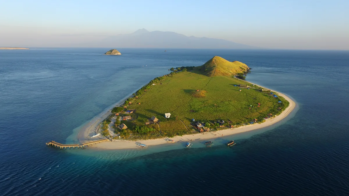 Aerial view of Kenawa Island’s grassy hill, curved sandy shoreline and surrounding blue sea