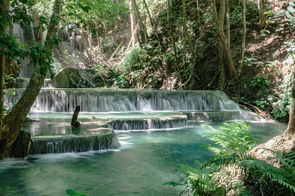 Tiered limestone pools and flowing water beneath forest trees at Mata Jitu Waterfall on Moyo Island