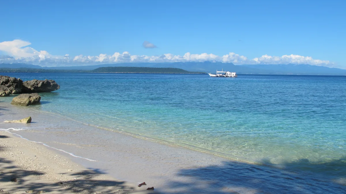 Clear shallow water and a sandy shore off Moyo Island, with a boat in the distance